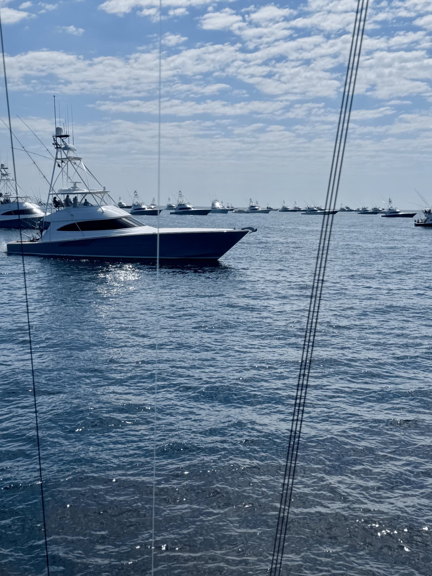 A sport-fisher cuts past the fleet, seen through the rigging of Big Daddy's