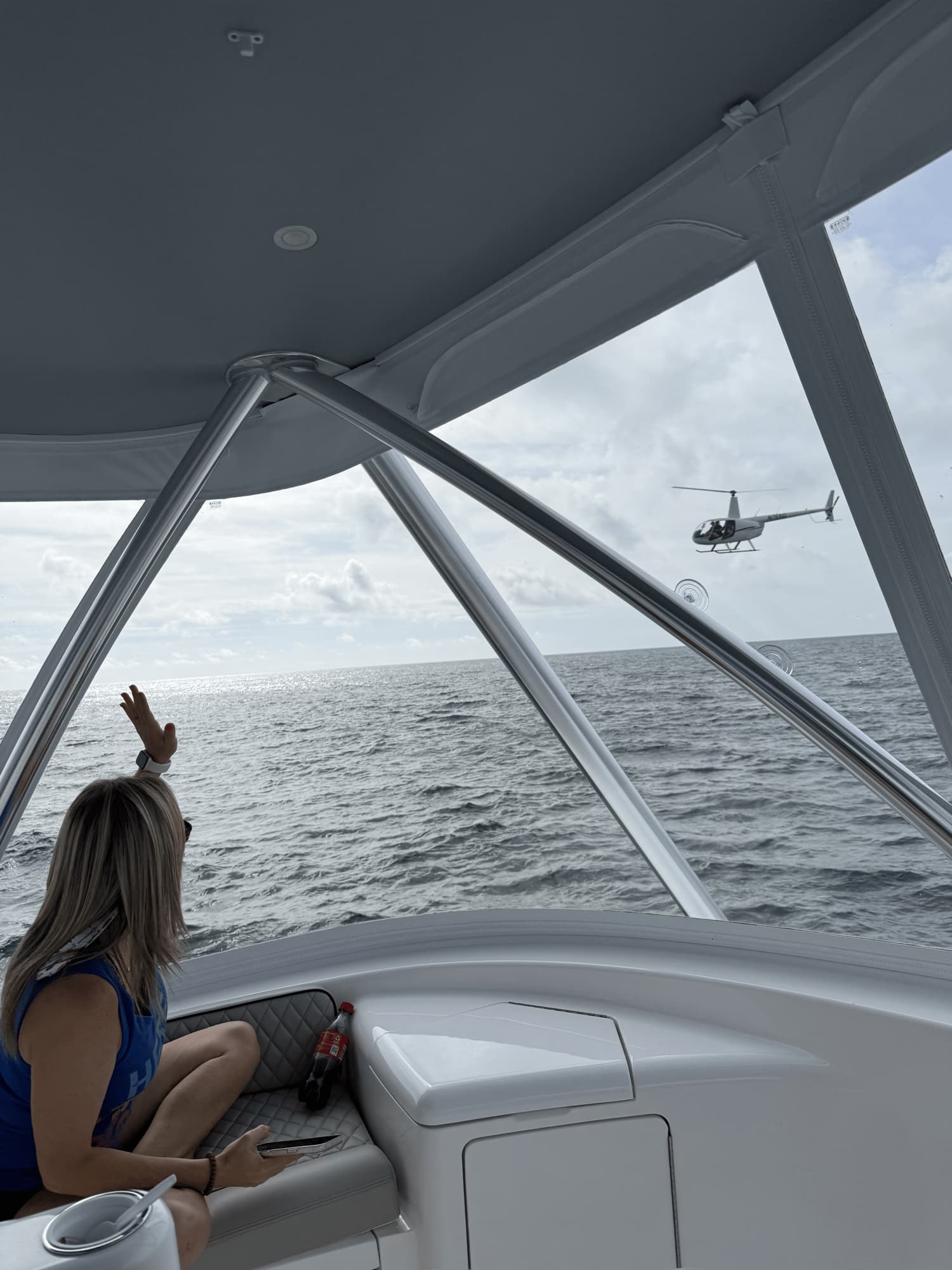 Crew member waves up at a helicopter buzzing the cockpit on a calm day